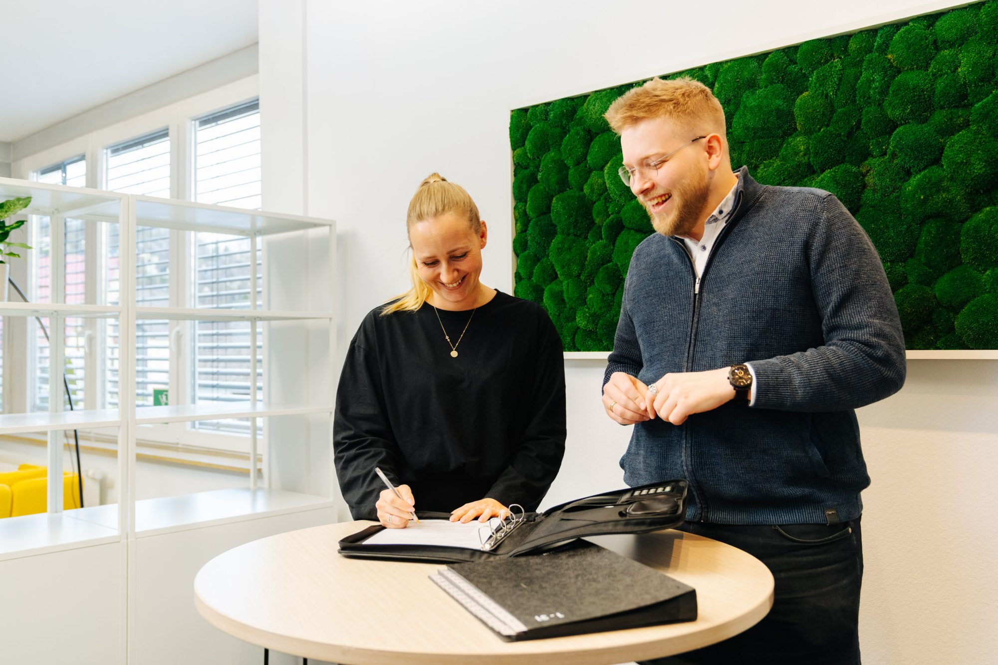 Two Carenetic employees laughing while filling in documents at a standing table