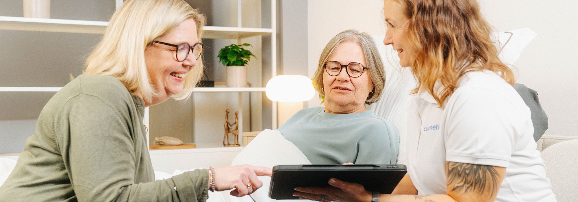 Carenetic Mitarbeiterin berät eine Patientin und ihre Angehörige mit einem Tablet
