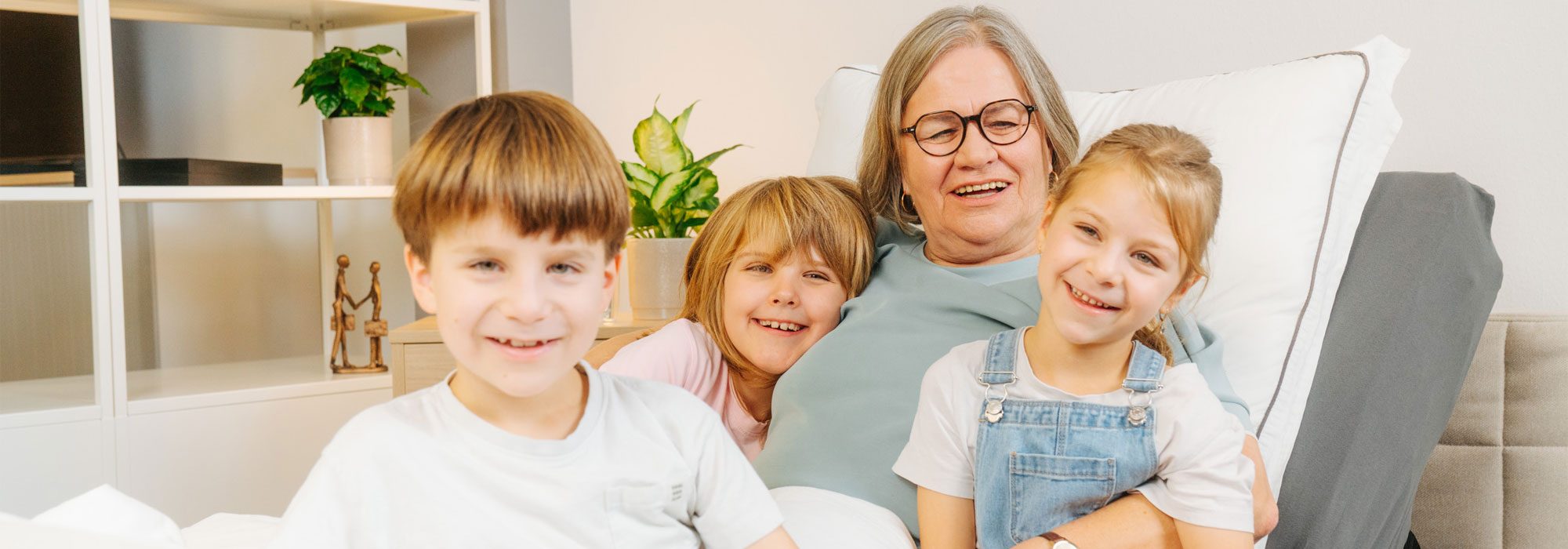 Elderly woman in a care bed with three laughing grandchildren