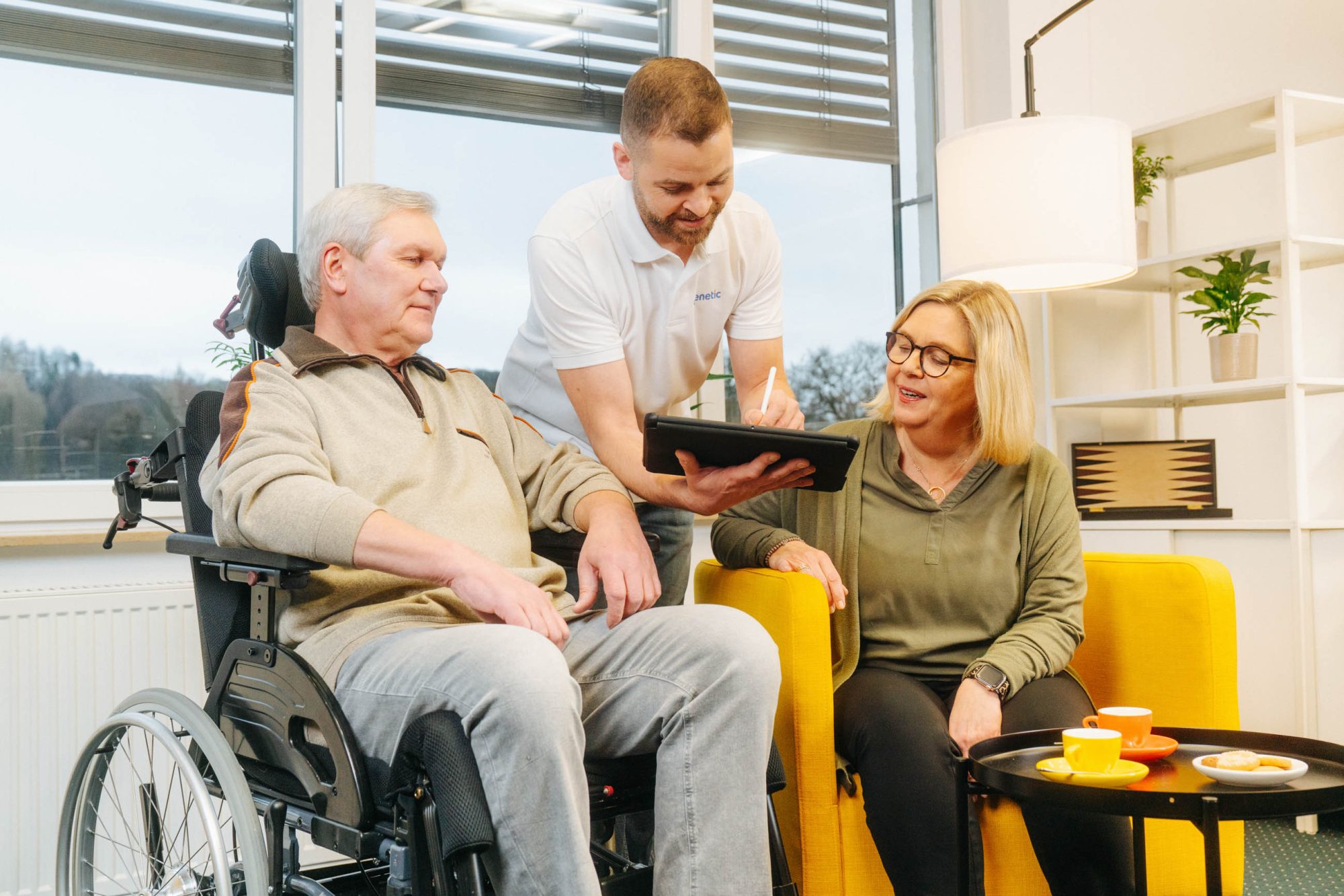 Carenetic employee showing information on a tablet to a man in a wheelchair and his relative