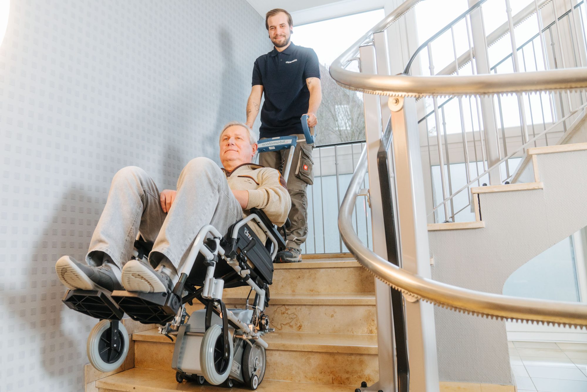 Carenetic employee taking a man in a wheelchair up a staircase with a stair climber