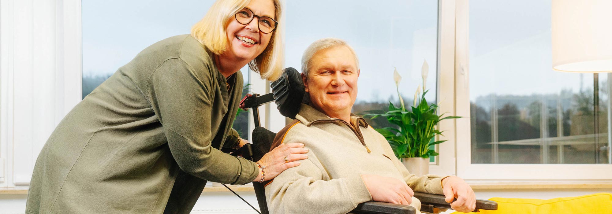 Family carer standing smiling next to an elderly man in a wheelchair