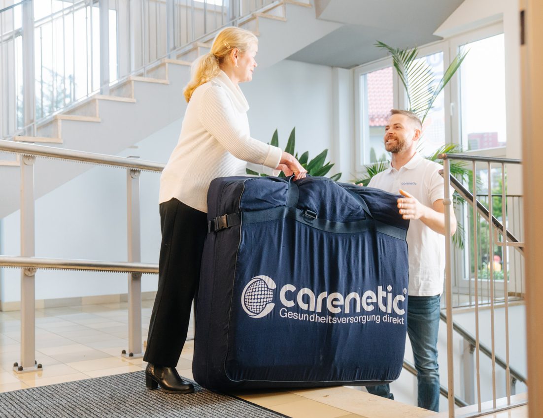 Carenetic-Mitarbeiter übergibt einer Angehörigen eine Antidekubitus-Matratze in der Transporttasche